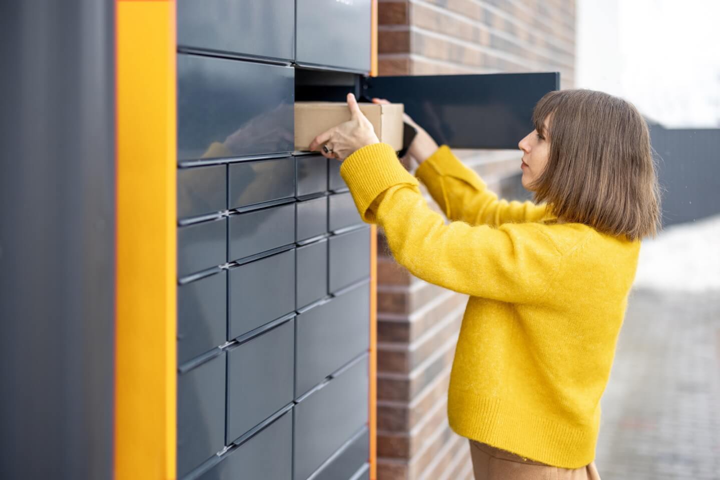 Woman getting parcel from cell of automatic post terminal outdoors
